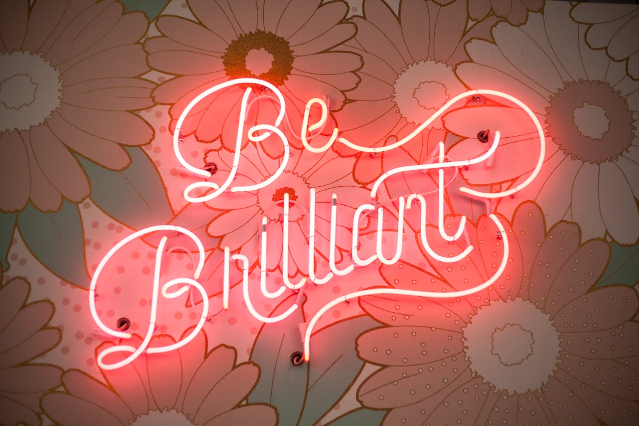 services-02 A glowing neon sign reading 'Be Brilliant' against a floral backdrop creates a vibrant and motivational atmosphere.